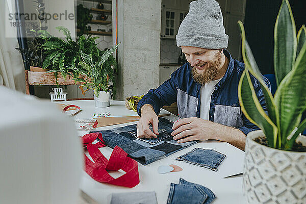 Fröhlicher Modedesigner näht Tasche auf Einkaufstasche in Werkstatt