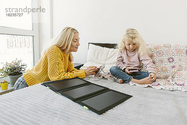 Lächelnde Mutter benutzt Tablet-PC mit Solarbatterieladegerät auf dem Bett