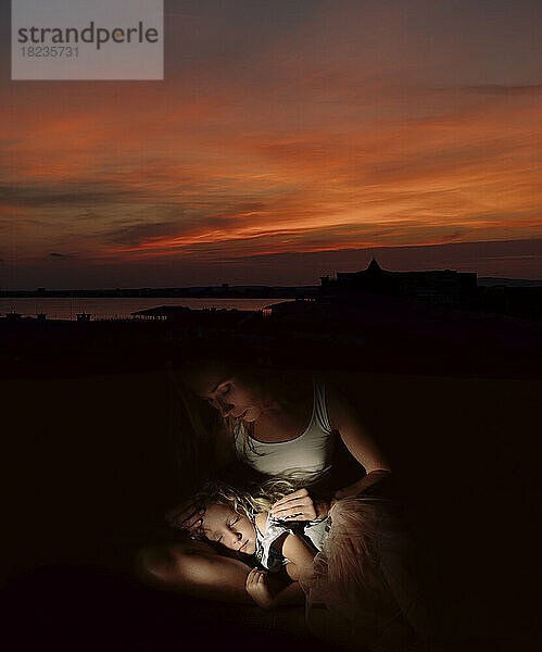 Frau vor schlafender Tochter bei Sonnenuntergang