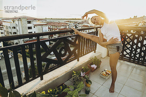 Frau macht Dehnübungen auf der Dachterrasse bei Sonnenuntergang