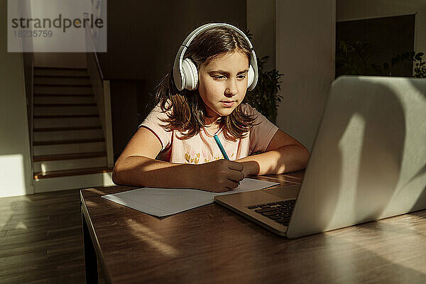 Mädchen mit kabellosen Kopfhörern beim E-Learning am Laptop zu Hause