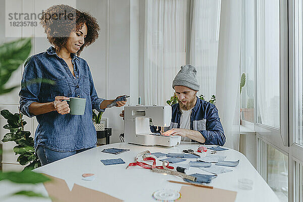 Modedesigner arbeitet an Nähmaschine mit Kollege und untersucht Denim-Stoff in Werkstatt