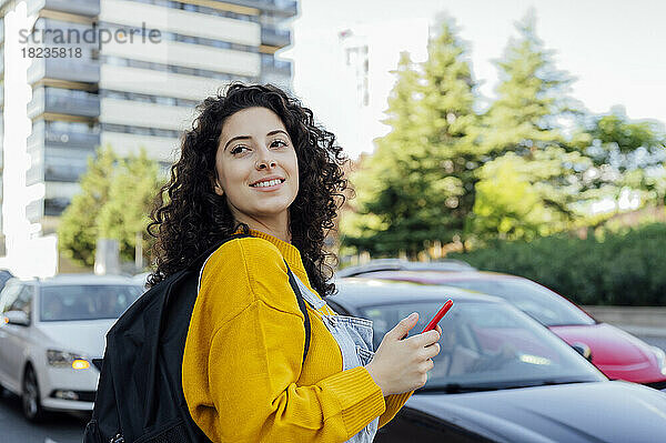 Lächelnde Frau mit Rucksack und Mobiltelefon unterwegs