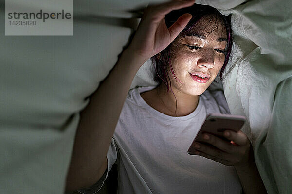 Lächelnde Frau benutzt Smartphone unter Decke zu Hause
