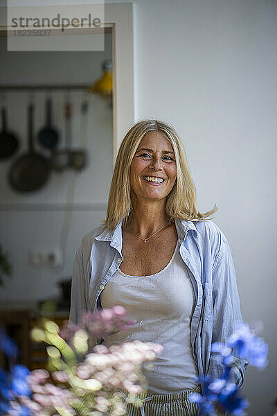 Happy mature woman with blond hair standing at home