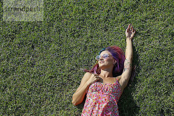 Lächelnde Frau liegt auf Gras und genießt den sonnigen Tag