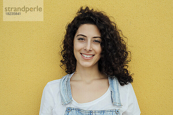 Schöne lächelnde Frau mit lockigem Haar vor gelber Wand