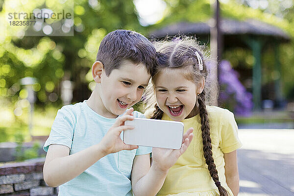 Glücklicher Bruder und Schwester  die ihr Smartphone im Garten benutzen