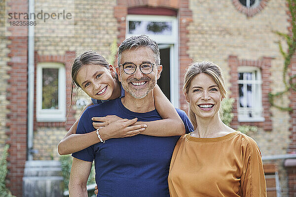 Lächelndes Mädchen mit Vater und Mutter vor dem Haus