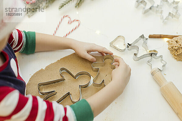Hands of boy using cookie cutter on gingerbread dough in kitchen