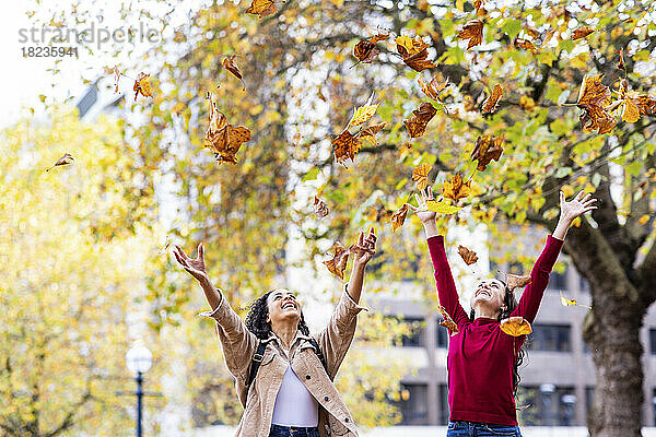 Glückliche junge Frauen werfen Herbstblätter und genießen es im Park