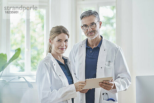 Lächelnde Ärzte stehen mit Tablet-PC in der Arztpraxis