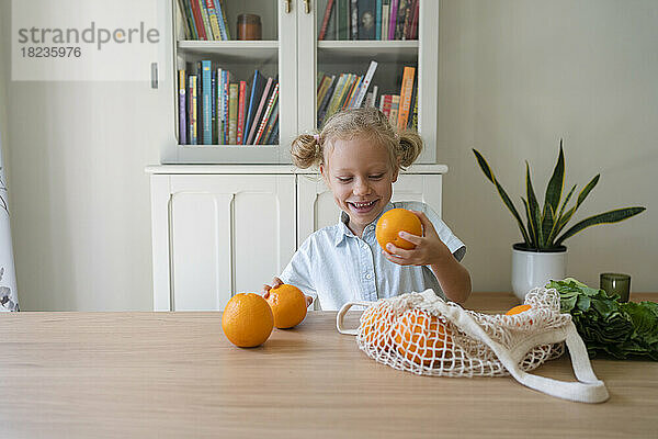 Glückliches blondes Mädchen mit Orangen  das am Tisch sitzt