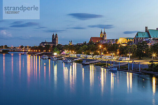 Deutschland  Sachsen-Anhalt  Magdeburg  Boote am Ufer der Elbe in der Abenddämmerung mit Stadtgebäuden im Hintergrund