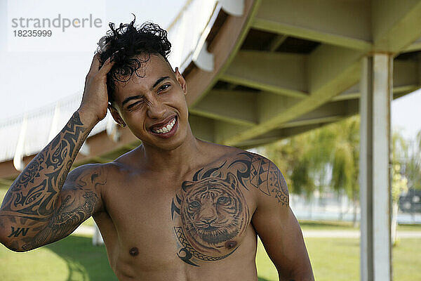 Happy shirtless young man with tattoos winking eye