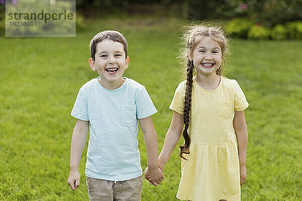 Fröhlicher Bruder und Schwester halten sich an den Händen und stehen im Garten