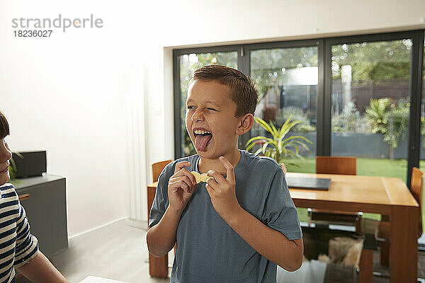 Verspielter Junge streckt die Zunge heraus und hält ungebackene Kekse zu Hause