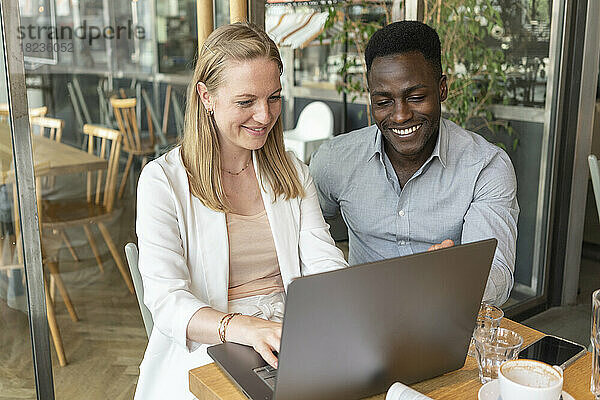 Glückliche Geschäftsfrau  die mit einem Kollegen im Café am Laptop arbeitet