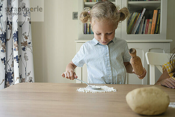 Lächelndes Mädchen mit Mehl auf dem Tisch zu Hause