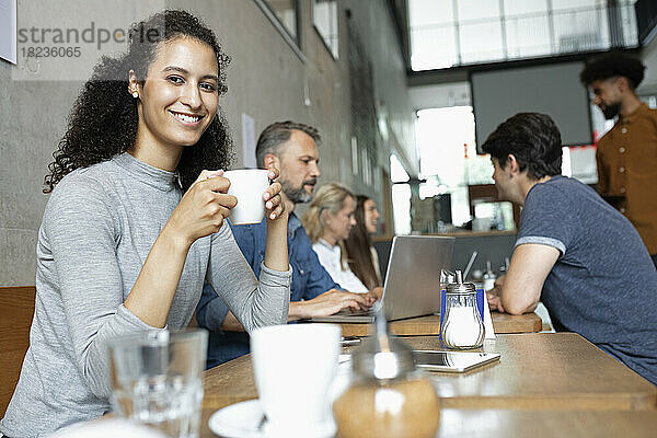 Lächelnde Frau trinkt Kaffee von Kunden im Café
