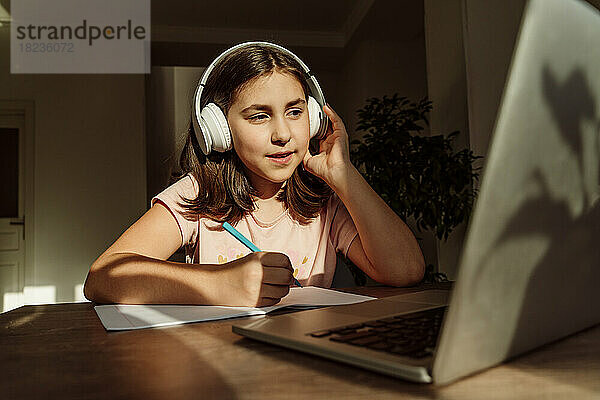 Mädchen mit kabellosen Kopfhörern lernt am Laptop am Schreibtisch