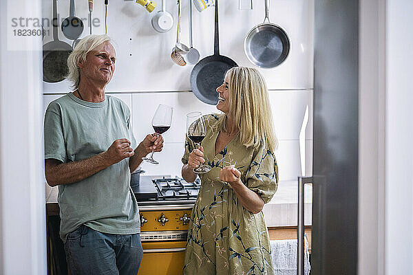 Glückliche reife Frau mit Mann  der in der Küche ein Glas Rotwein hält