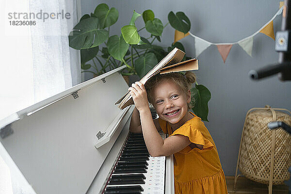 Nettes lächelndes Mädchen mit Noten am Klavier zu Hause