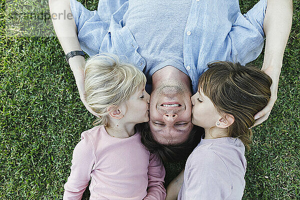 Daughters kissing father on cheeks and relaxing in grass