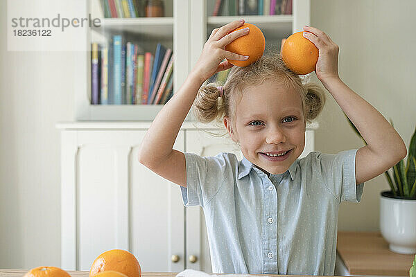 Verspieltes Mädchen mit Orangen auf dem Kopf zu Hause