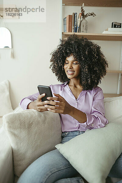 Lächelnde Frau  die zu Hause auf dem Sofa sitzt und ihr Smartphone benutzt