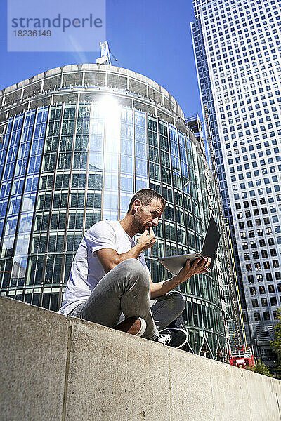 Mann benutzt Laptop an sonnigem Tag in der Stadt