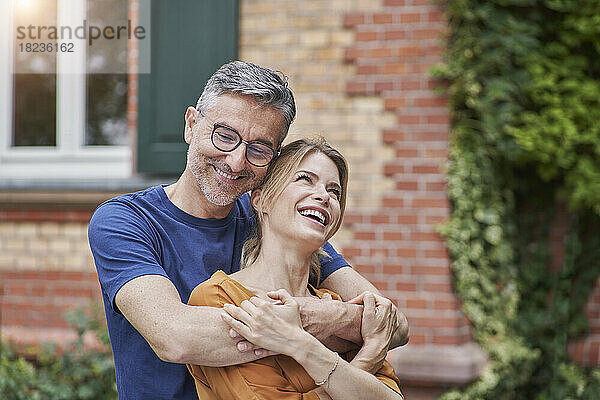 Lächelnder Mann umarmt glückliche Frau vor dem Haus
