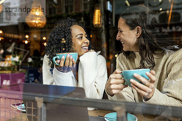 Glückliche Frau spricht mit einer Freundin  die im Café eine Tasse hält