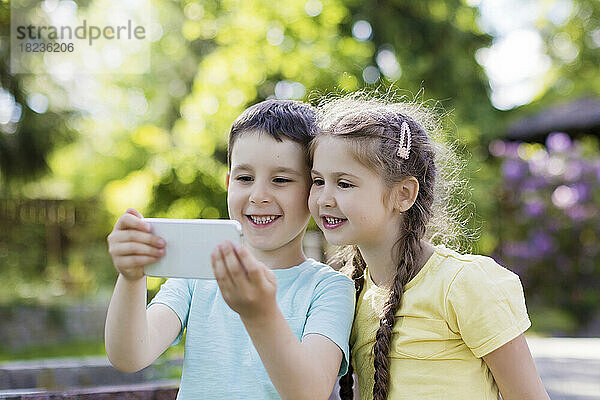 Lächelnder Bruder und Schwester benutzen Smartphone im Hinterhof