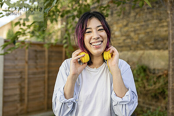 Glückliche junge Frau mit Kopfhörern steht im Garten