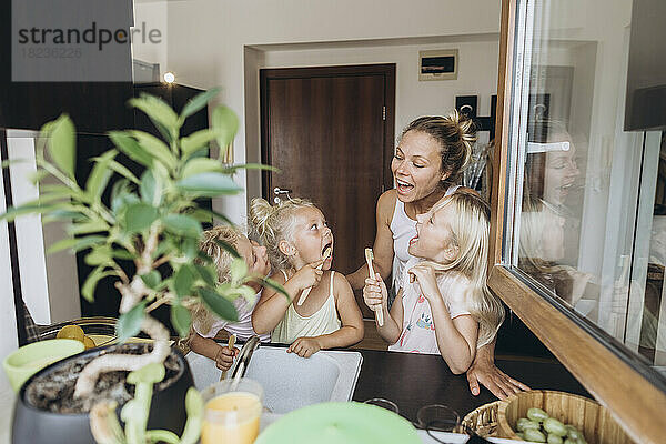 Mutter beobachtet Töchter beim Zähneputzen mit Holzbürsten in der Küche