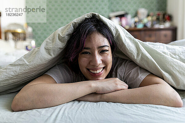 Glückliche Frau entspannt sich zu Hause auf dem Bett mit Decke