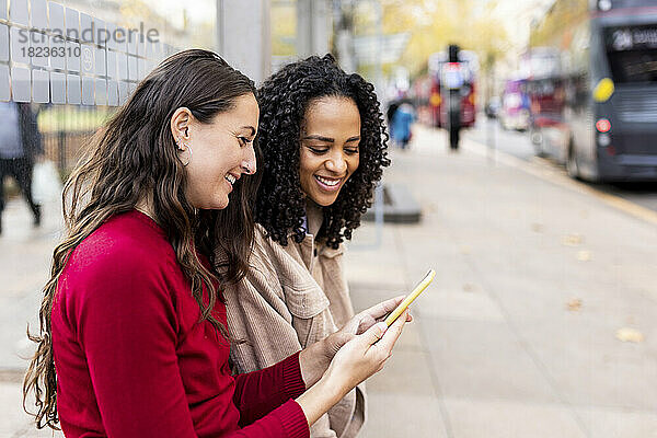 Frau teilt Smartphone mit Freundin am Fußweg