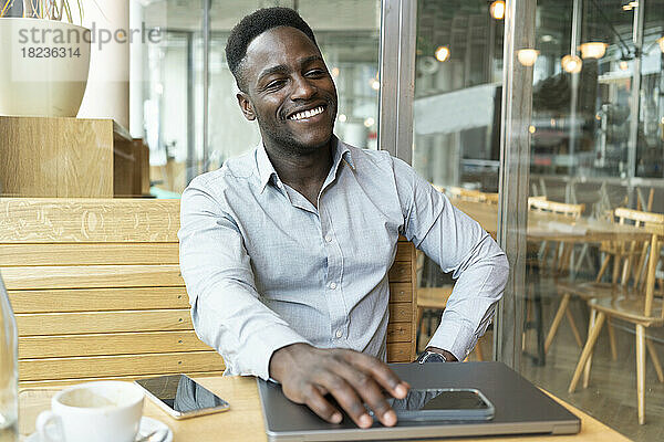 Glücklicher Geschäftsmann sitzt mit Laptop und Smartphone im Café