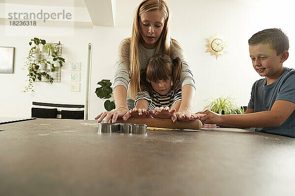 Mädchen hilft Schwester beim Teigrollen von Bruder zu Hause