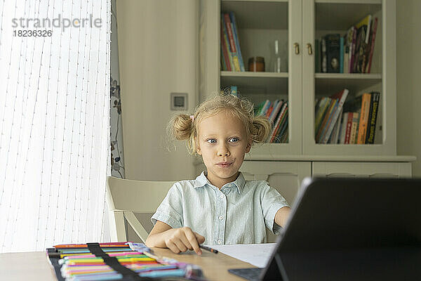 Überraschtes blondes Mädchen benutzt Laptop am Schreibtisch
