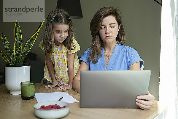 Geschäftsfrau arbeitet am Laptop  Tochter steht zu Hause am Schreibtisch