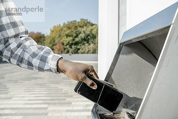 Hand eines Mannes  der Mobiltelefone in die Mülltonne wirft