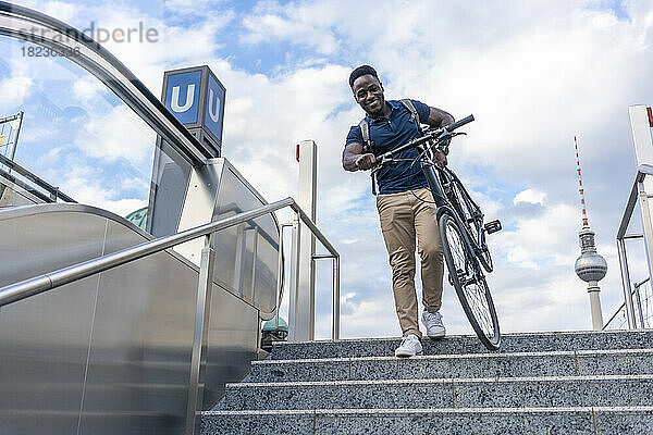 Lächelnder Mann  der Fahrrad auf Stufen trägt
