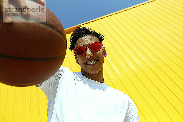 Lächelnder Mann mit Basketball vor gelber Wand