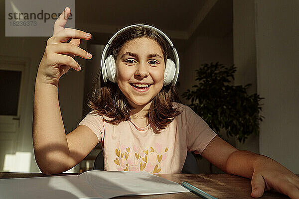 Fröhliches Mädchen mit kabellosen Kopfhörern sitzt am Schreibtisch