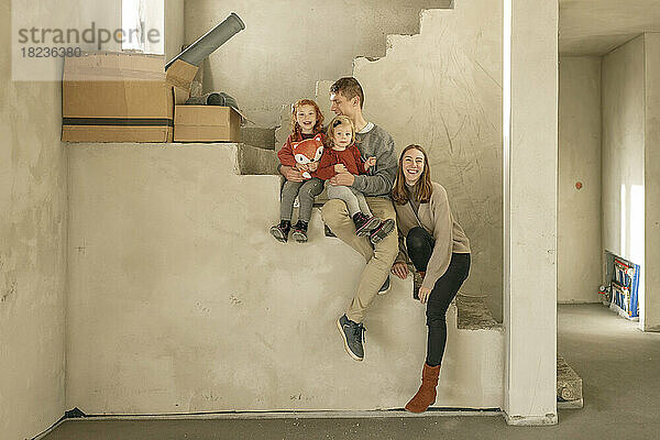Glückliche Familie sitzt auf der Treppe eines unvollständigen Hauses