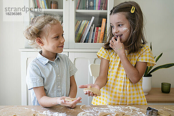Glückliche Mädchen bereiten zu Hause Kekse mit Teig auf dem Tisch zu