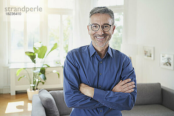 Happy man wearing eyeglasses with arms crossed at home