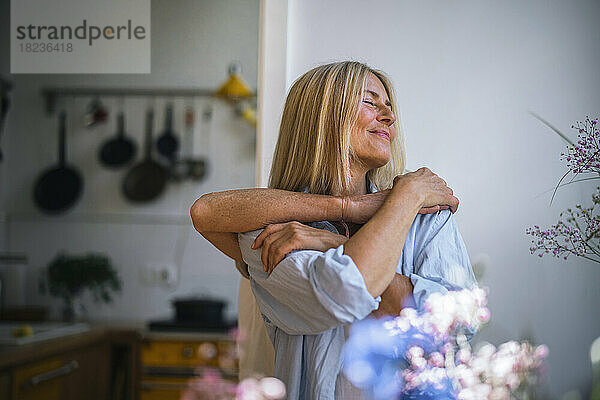 Lächelnde blonde Frau mit Freund  der sie zu Hause von hinten umarmt